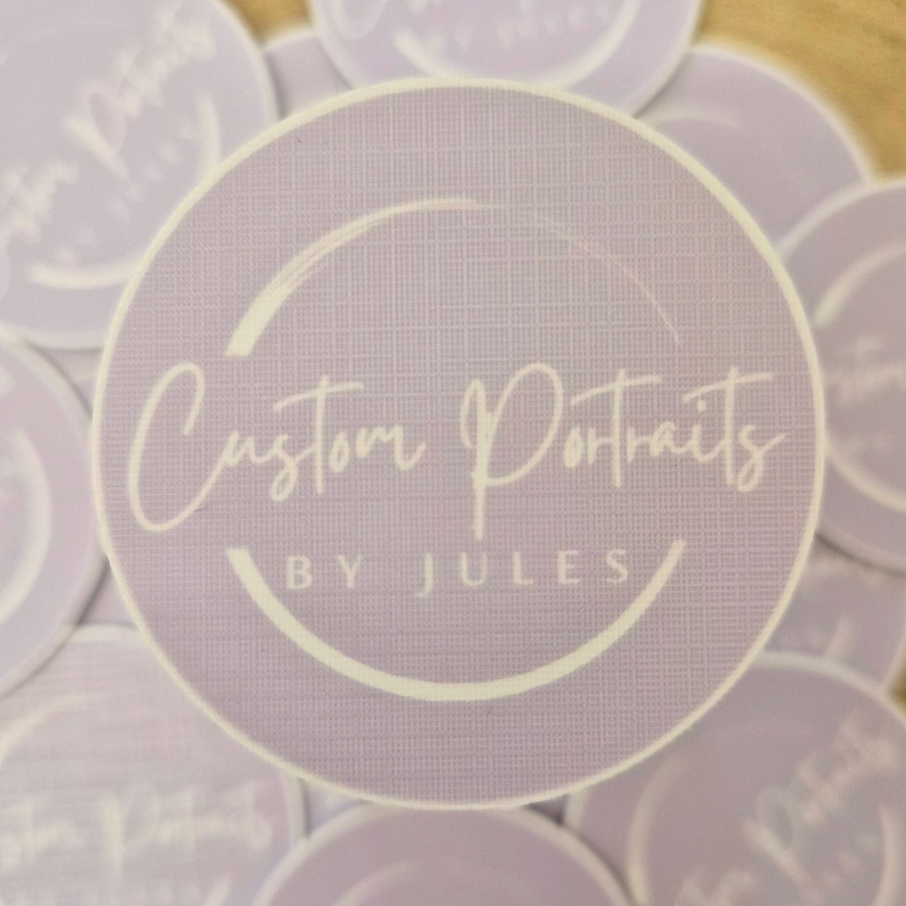 Round purple stickers with 'Custom Portraits by Jules' text on a wooden surface